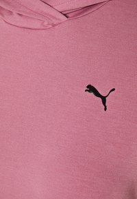 Różowy sweter z gładką fakturą, z czarnym logo Pumy na piersi i z kapturem ze sznurkiem do regulacji dopasowania.
