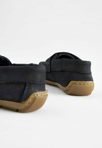 Scarpe slip-on nere in suede con una parte superiore ruvida, cuciture blu navy a contrasto e suole in gomma marrone con una presa a motivo.