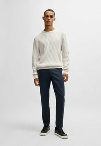 Pullover lavorato a maglia di crema chiara con un motivo a rombi, abbinato a pantaloni scuri blu su misura e sneakers nere basse.