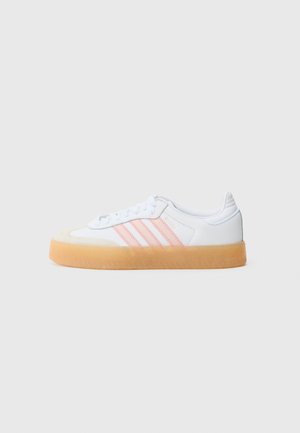 White sneakers with pink stripes, rubber sole, and suede toe cap. Features lace closure and textured materials on the upper.