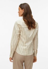 Pikad varrukad, kreemikas triiksärk, millel on vertikaalsed triibud helepruunis ja tumepunas. Varustatud nööpidega mansettidel ja detailse seljaosaga.