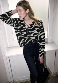 Blusa a righe zebrate bianco e nero con scollatura a V e dettaglio con fiocco, abbinata a jeans scuri attillati e una piccola borsa nera.