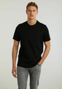 Tricou negru din bumbac, cu mâneci scurte, guler rotund și un logo mic, negru, pe piept. Asortat cu blugi gri deschis.
