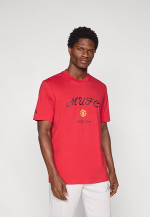 T-shirt en coton rouge avec le texte "MUFC" en noir, logo du club et détail "Old Trafford". Manches courtes et col rond. Design simple.