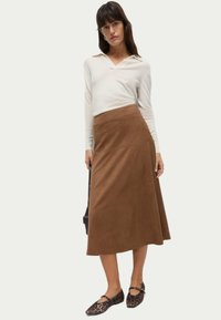 Falda maxi de ante marrón con una textura suave, diseño acampanado y cintura alta. Combinada con una blusa blanca de manga larga y zapatos planos de estampado de leopardo.