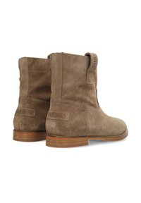 Botas de tobillo de ante marrón con un bajo tacón de madera, que cuentan con una lengüeta de agarre y un detalle de la marca en relieve en el lado. Textura suave y diseño minimalista.