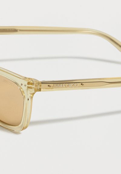 Ημιδιαφανή κίτρινα ορθογώνια γυαλιά ηλίου με ανοιχτά καφέ φακούς και χαραγμένο το «JIMMY CHOO» στο πλάι.