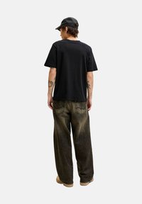 Zwarte t-shirt met korte mouwen in combinatie met een brede, donkere denim jeans. De outfit wordt compleet gemaakt met een zwarte pet en beige schoenen.