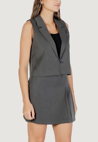 Blazer grigio senza maniche con rever e chiusura a un bottone, abbinato a una gonna coordinata in tessuto liscio dal taglio leggermente svasato.