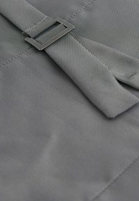 Close-up of grey textured fabric with a matching strap threaded through a rectangular metal buckle.