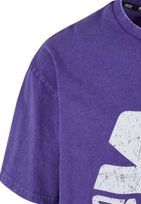T-shirt en coton violet avec un col rond et des manches courtes. Présente un grand motif blanc usé sur le devant.