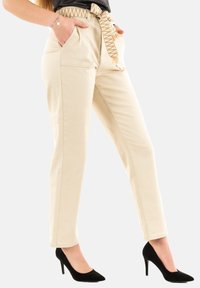 Pantaloni beige a vita alta, con tasche laterali e una cintura a strisce in marrone e crema. Indossati con scarpe con tacco alto nere.