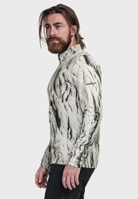 Langärmliges, mit Reißverschluss versehenes Oberteil in einem marmorähnlichen Muster, das eine Mischung aus Schwarz und Cremefarben zeigt. Das Logo auf dem linken Ärmel ist sichtbar.