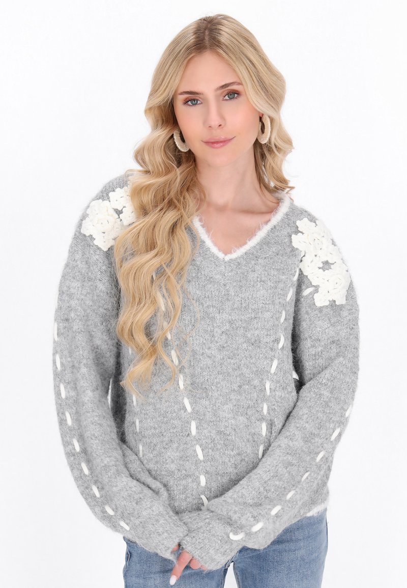 Grauer Strickpullover mit V-Ausschnitt, ausgestattet mit weißen Blumenapplikationen an den Schultern und kontrastierender Stickerei entlang der Ärmel.