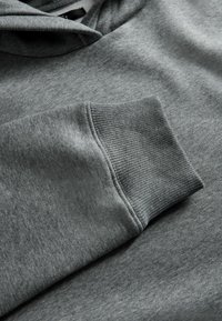 Szara bluza z kapturem o miękkiej fakturze, z prążkowanymi mankietami i regulowanym kapturem; widok płaski podkreślający detale rękawów i jakość materiału.