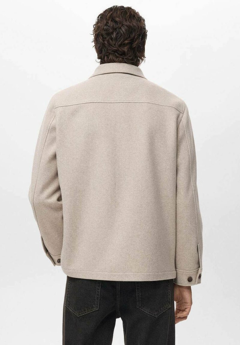 Giacca in misto lana beige con collo a camicia e polsini abbottonati, caratterizzata da una linea dritta e un design minimalista.