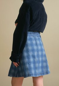 Modrá kostkovaná džínsová sukně s volným střihem, knoflíkovými detaily a vysokým pasem; v kombinaci s tmavě námořnickým kordovým topem.
