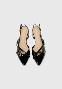 Černé lakované boty typu slingback s špičatou špičkou, křížovou designovou páskou a zlatými sponami. Hladké vnitřní podšívání.