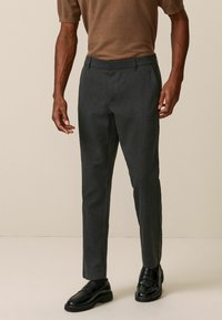 Pantalon gris ajusté en tissu texturé, avec un design slim et des poches latérales discrètes, associé à des mocassins noirs.