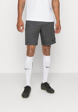 Graue Sportsshorts mit einem schwarzen Nike-Logo, kombiniert mit weißen knielangen Socken mit schwarzen Streifen und schwarzen Fußballschuhen.