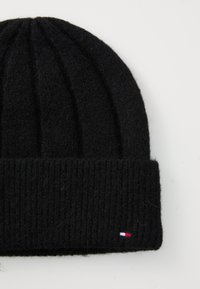 Căciulă tricotată neagră cu textură rib guvernată, având o margine pliată și un logo mic, colorat pe lateral. Material moale și cald.