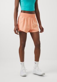 Shorts pêches avec une taille élastique, présentant une coupe décontractée et une texture lisse, associés à des baskets blanches et des chaussettes de sport.