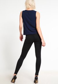 Námornická bezrukávová top s kulatým výstřihem, v kombinaci s černými skinny džíny a černými vysokými podpatky, z pohledu zezadu.