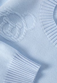 Pull en maille bleu clair avec col et poignets côtelés, présentant des détails texturés et un motif en relief. Texture de tissu douce.