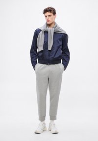 Tengerészkék bomberdzseki geometriai mintával, szürke kötött sállal és világos szürke, mandzsettás szabadidőnadrággal. A tornacipők fehér és krémszínű árnyalatúak.