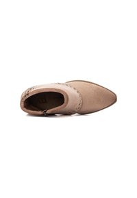 Botín beige de ante, con punta afilada, tachuelas decorativas plateadas a lo largo de la costura y un cierre lateral con cremallera.