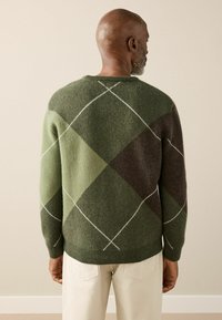 Green wool sweater with a diamond pattern in varying shades of green and brown, featuring white stitching along the seams.