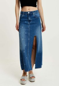 Denim maxi skirt with a front slit, light blue wash, and polka dot pattern. Features a fitted waist and classic five-pocket design.