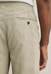 Khaki spodnie o gładkiej fakturze, z tylną kieszenią i zapięciem na guzik. Klasyczny design z minimalistycznymi detalami szycia.