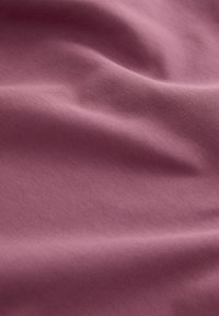 Tissu doux et texturé de couleur mauve atténuée, avec des plis délicats et une finition lisse, suggérant un matériau léger et respirant.