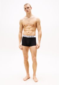 Caleçons boxers noirs avec une taille blanche affichant "HILFIGER" en lettres noires. Le tissu est lisse, ajusté et extensible.