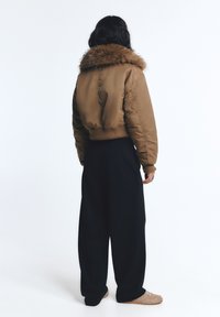 Bruine cropped pufferjack met een bontkraag; hoge nek; geribbelde mouwen; gecombineerd met zwarte brede broek; schoenen in neutrale tinten.