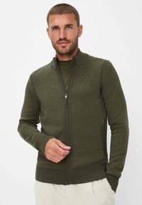 Olivgrüner Reißverschluss-Pullover aus weichem Strickmaterial. Mit hohem Kragen und gerippten Bündchen und Saum, hat er eine glatte Textur und eine taillierte Passform.