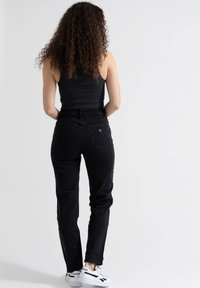 Jeans pretos de cintura alta com perna afunilada, bolsos traseiros e um acabamento texturizado, combinados com uma t-shirt canelada preta e ténis brancos.