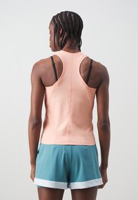 Top sportiv de culoare piersică cu design racerback, textură moale și bretele contrastante negre. Asortat cu pantaloni scurți teal cu dantelă albă.