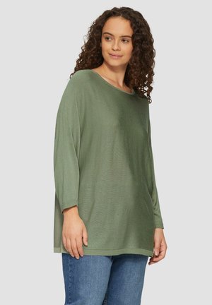 Oversized, lange mouwen trui in gedempt groen, gemaakt van textuurstof, met een ronde halslijn en ribgebreide onderrand. Gecombineerd met blauwe jeans.