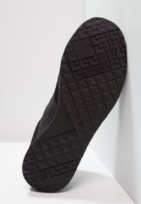 Black sneaker sole with textured, patterned grip, featuring a textured black upper and a smooth side profile.