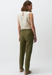 Beige, rückenfreies Leinenoberteil, kombiniert mit olivgrünen, elastischen Hosen. Weiche Textur, einfaches Design und neutrale Farbpalette.