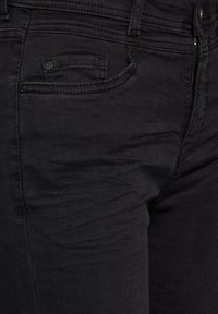 Jeans de mezclilla negra con un diseño clásico de cinco bolsillos, textura suave y sutiles detalles de costura, con apertura de cremallera.