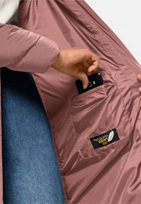 Rosa isolierte Jacke mit angenehmer, glänzender Oberfläche; verfügt über eine Tasche, in der ein Smartphone gehalten wird; Etikett besagt "hochwertige Daunen 700."