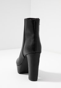 Black leather ankle boot featuring a high stiletto heel and smooth texture. The rear view highlights minimalistic design and clean lines.