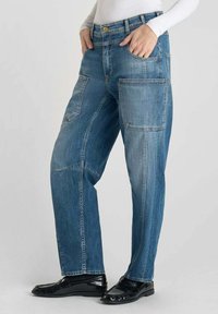 Jeans en denim bleu clair avec une coupe ample, dotés de poches plaquées, d'une taille haute, de détails de boutons dorés et d'accents de couture visibles.