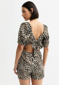 Leopardmönstrad jumpsuit med korta puffärmar, öppen rygg med rosettdetalj och elastisk midja. Mjukt tyg med svarta och bruna fläckar.