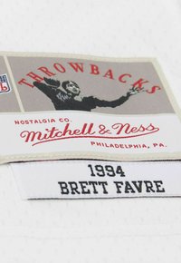 Throwbacks Mitchell & Ness label with a football player silhouette and sewn tag reading "1994 Brett Favre" on white fabric.