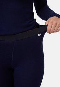 Marinblå leggings visas med en dragning vid midjan, tillverkade av mjukt, stretchigt material med ett svart elastiskt band och en liten logotypetikett.