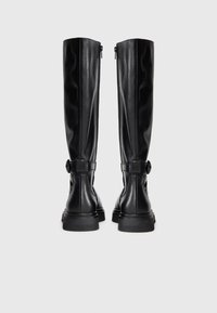 Un paio di stivali alti in pelle nera con cerniere laterali e cinturini decorativi, mostrati da dietro su uno sfondo bianco semplice.
